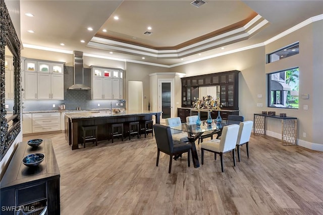 dining space with light wood-type flooring, a tray ceiling, and ornamental molding