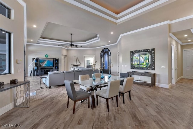 dining room with a tray ceiling, crown molding, ceiling fan, and light wood-type flooring