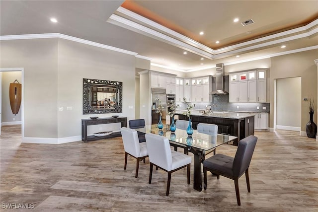 dining area featuring a tray ceiling, sink, light hardwood / wood-style floors, and ornamental molding