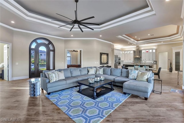 living room featuring light wood-type flooring, a raised ceiling, ceiling fan, and crown molding