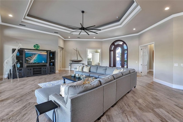 living room featuring light wood-type flooring, a tray ceiling, ceiling fan, and crown molding