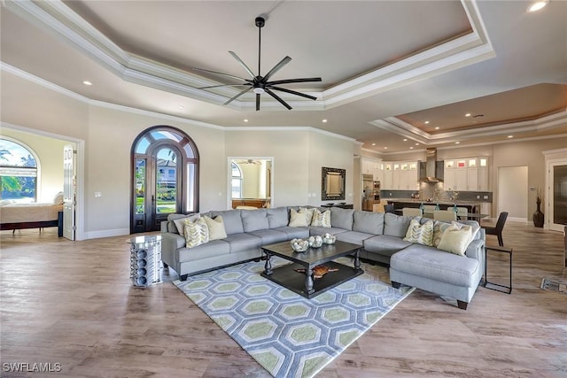 living room featuring a raised ceiling, ceiling fan, and ornamental molding