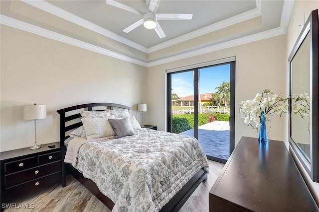 bedroom featuring access to exterior, light wood-type flooring, ornamental molding, a raised ceiling, and ceiling fan