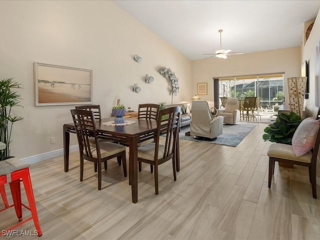 dining space featuring a high ceiling, ceiling fan, light wood-style flooring, and baseboards