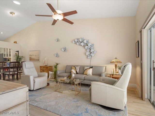 living room with ceiling fan, light hardwood / wood-style flooring, and vaulted ceiling