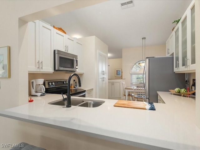 kitchen with pendant lighting, white cabinets, sink, kitchen peninsula, and stainless steel appliances