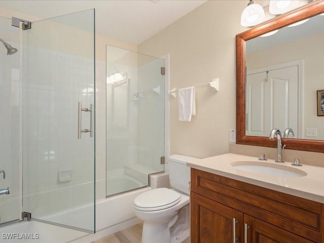 full bathroom with wood-type flooring, vanity, bath / shower combo with glass door, and toilet