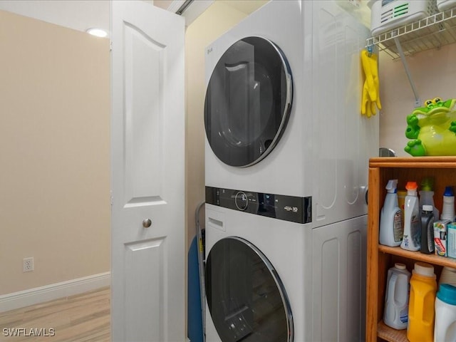 clothes washing area featuring laundry area, wood finished floors, stacked washer and clothes dryer, and baseboards