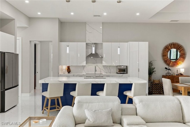 kitchen featuring decorative backsplash, stainless steel fridge, wall chimney exhaust hood, decorative light fixtures, and white cabinetry