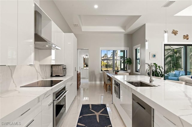 kitchen with appliances with stainless steel finishes, sink, wall chimney range hood, decorative light fixtures, and white cabinetry