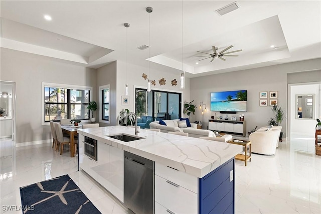 kitchen with white cabinetry, sink, hanging light fixtures, a raised ceiling, and an island with sink