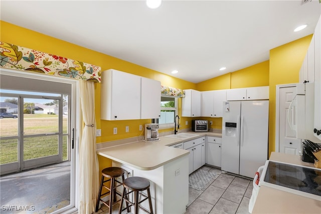 kitchen featuring vaulted ceiling, white cabinetry, sink, a breakfast bar area, and white appliances