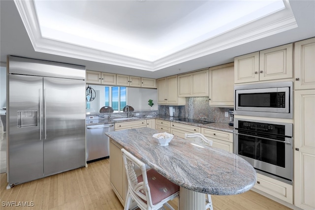 kitchen featuring built in appliances, light stone counters, a tray ceiling, and a breakfast bar