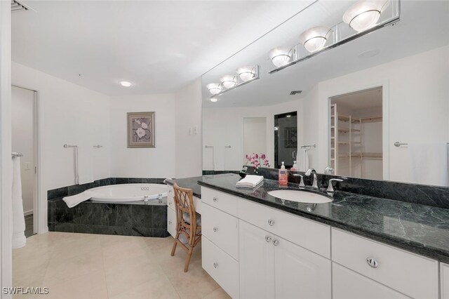 bathroom with tile patterned flooring, vanity, and a relaxing tiled tub