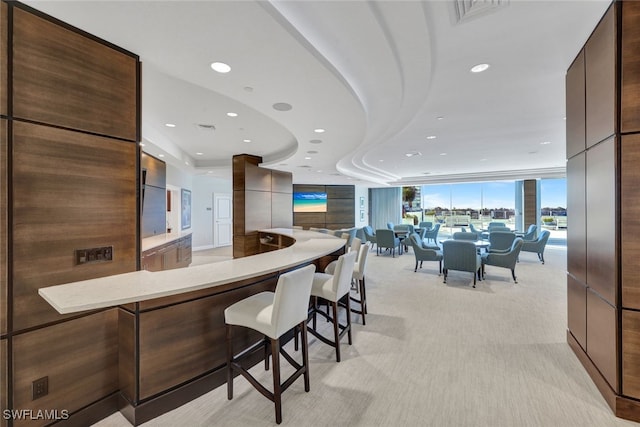 kitchen featuring a wall of windows, a kitchen breakfast bar, light stone counters, light carpet, and kitchen peninsula