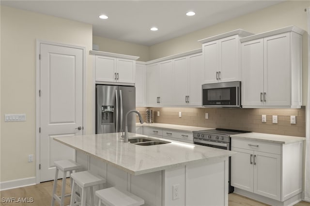 kitchen featuring a kitchen bar, sink, white cabinetry, appliances with stainless steel finishes, and an island with sink