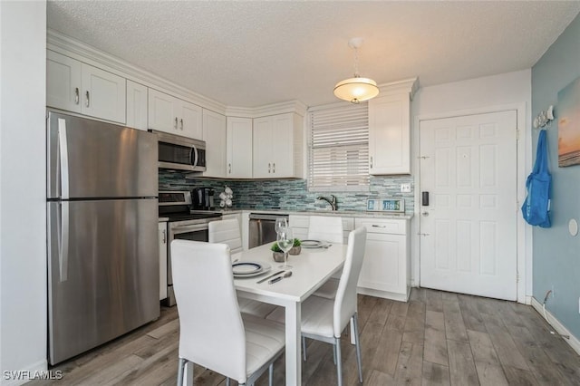 kitchen with stainless steel appliances, white cabinetry, and pendant lighting