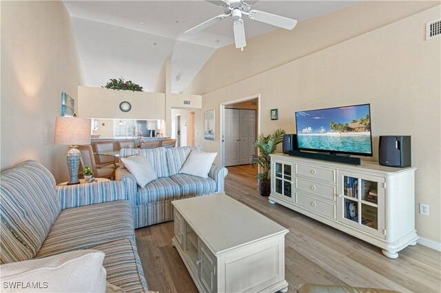 living room with ceiling fan, light hardwood / wood-style floors, and vaulted ceiling