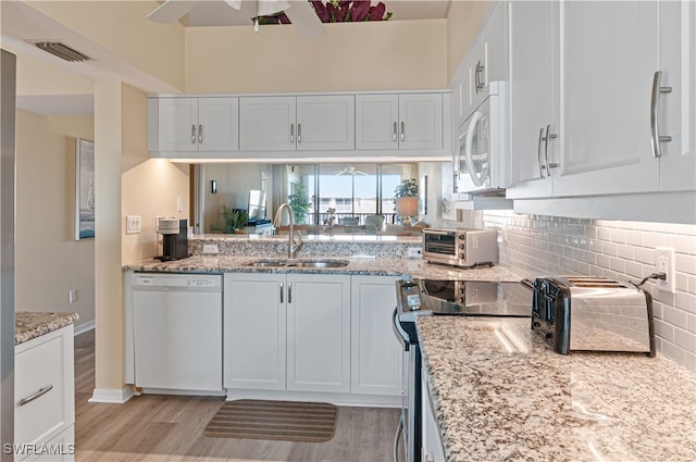 kitchen with tasteful backsplash, light stone counters, white appliances, sink, and white cabinets