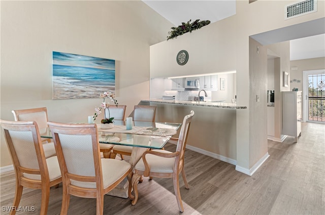 dining area featuring sink, high vaulted ceiling, and light wood-type flooring