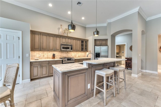 kitchen featuring stainless steel appliances, sink, decorative light fixtures, light stone counters, and a center island with sink