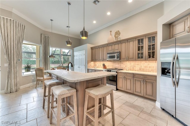 kitchen featuring light stone counters, hanging light fixtures, a center island with sink, decorative backsplash, and appliances with stainless steel finishes