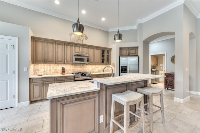 kitchen with a center island with sink, appliances with stainless steel finishes, light stone countertops, pendant lighting, and decorative backsplash