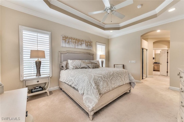 carpeted bedroom featuring ornamental molding, ceiling fan, a tray ceiling, and ensuite bathroom