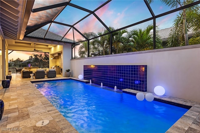 pool at dusk featuring pool water feature, a patio area, outdoor lounge area, and glass enclosure