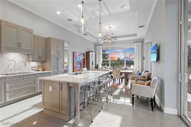 kitchen featuring pendant lighting, sink, a kitchen island with sink, a tray ceiling, and black electric cooktop