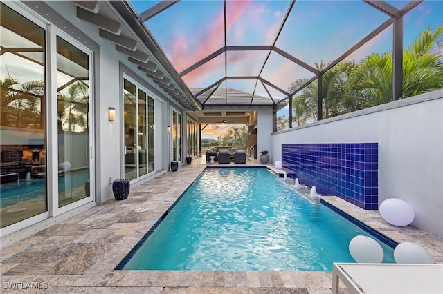 pool at dusk featuring a lanai, pool water feature, and a patio area