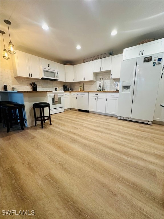 kitchen with white cabinetry, light hardwood / wood-style floors, white appliances, hanging light fixtures, and sink