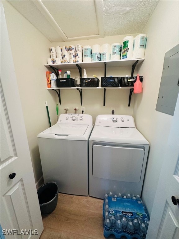 laundry area with a textured ceiling, electric panel, washing machine and clothes dryer, and hardwood / wood-style floors