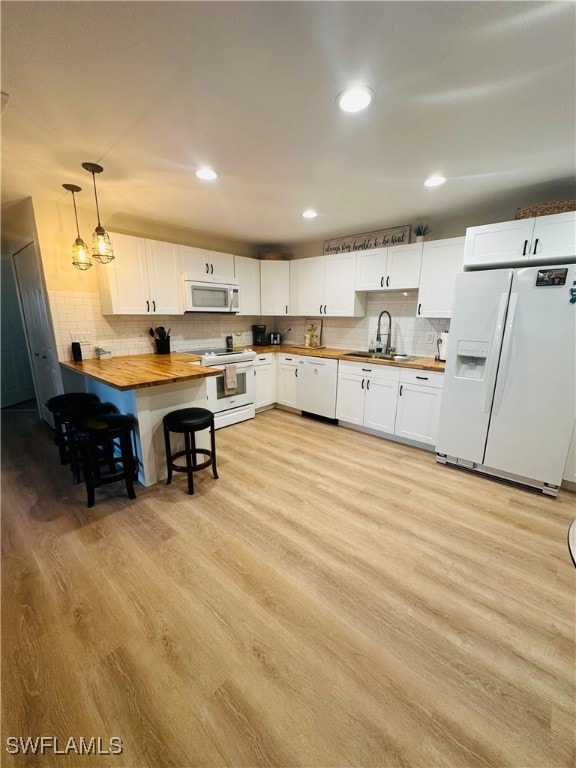 kitchen featuring pendant lighting, white appliances, white cabinets, wood counters, and sink