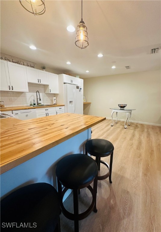 kitchen featuring decorative light fixtures, wooden counters, light hardwood / wood-style flooring, white refrigerator with ice dispenser, and white cabinets