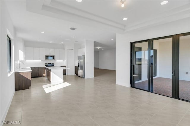 kitchen featuring stainless steel appliances, a raised ceiling, sink, white cabinets, and a kitchen island