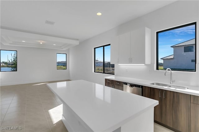 kitchen featuring stainless steel dishwasher, sink, white cabinets, a center island, and light tile patterned flooring