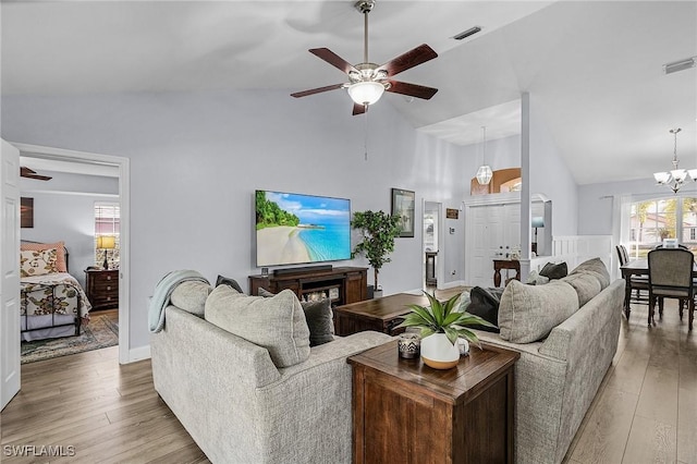 living room with high vaulted ceiling, ceiling fan with notable chandelier, and light hardwood / wood-style floors