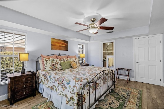 bedroom with hardwood / wood-style floors, ensuite bath, a raised ceiling, and ceiling fan