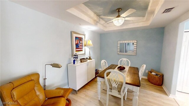 dining room featuring ceiling fan, light hardwood / wood-style floors, and a tray ceiling