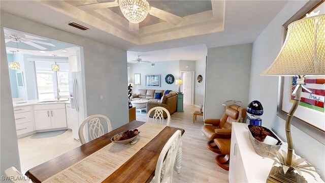 dining room with a raised ceiling, ceiling fan, and light hardwood / wood-style floors