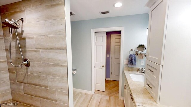 bathroom featuring tiled shower, hardwood / wood-style flooring, and vanity