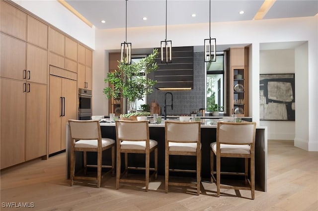 kitchen with stainless steel oven, light brown cabinets, paneled built in refrigerator, an island with sink, and light hardwood / wood-style floors