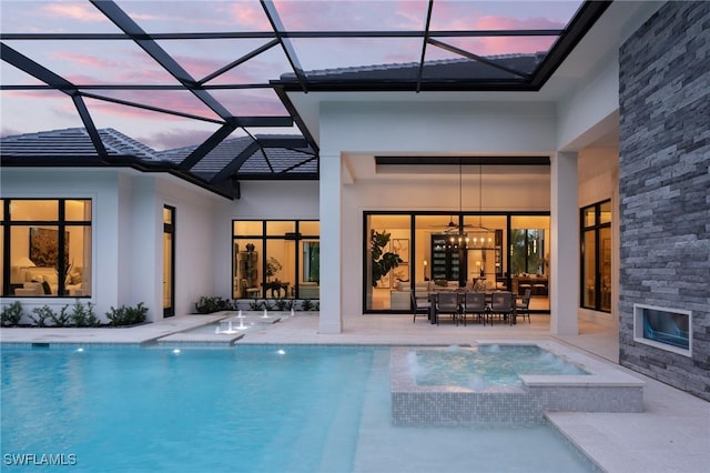 pool at dusk featuring an outdoor living space with a fireplace, a patio area, a lanai, and an in ground hot tub