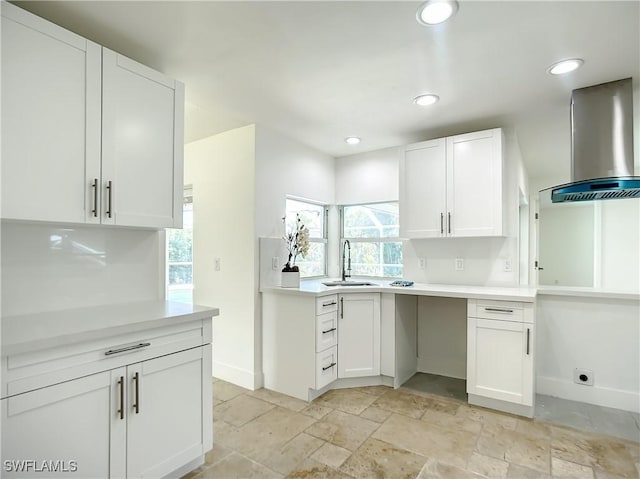 kitchen featuring wall chimney range hood, white cabinets, backsplash, and sink