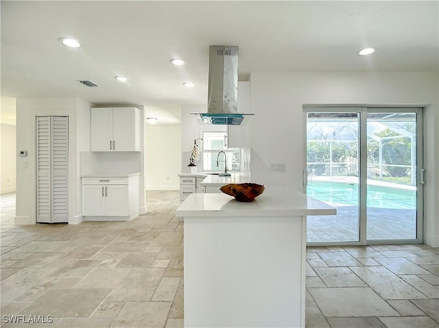 kitchen with kitchen peninsula, white cabinetry, sink, and island exhaust hood