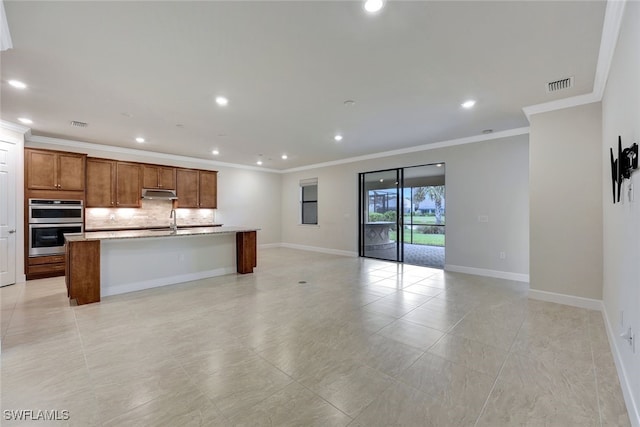 kitchen featuring sink, ornamental molding, a breakfast bar area, decorative backsplash, and a center island with sink