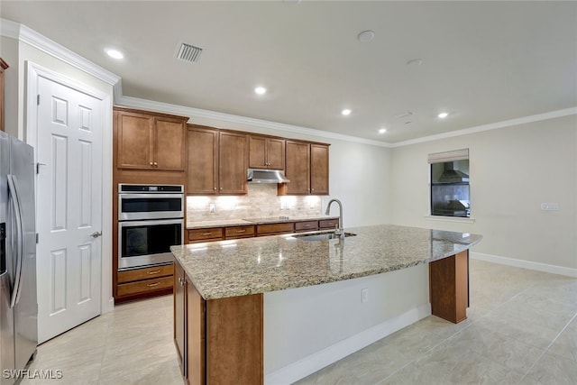 kitchen with sink, stainless steel appliances, light stone counters, decorative backsplash, and a center island with sink