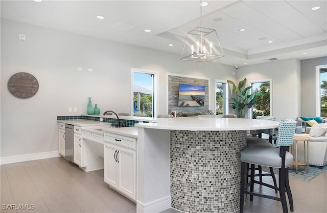 kitchen featuring pendant lighting, a notable chandelier, a kitchen bar, a tray ceiling, and white cabinetry