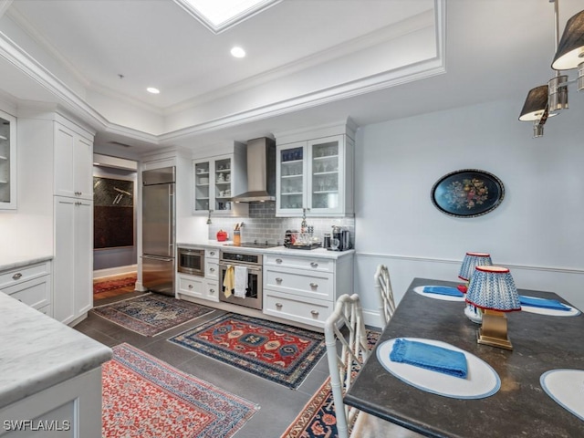 kitchen featuring white cabinets, appliances with stainless steel finishes, a tray ceiling, and wall chimney exhaust hood